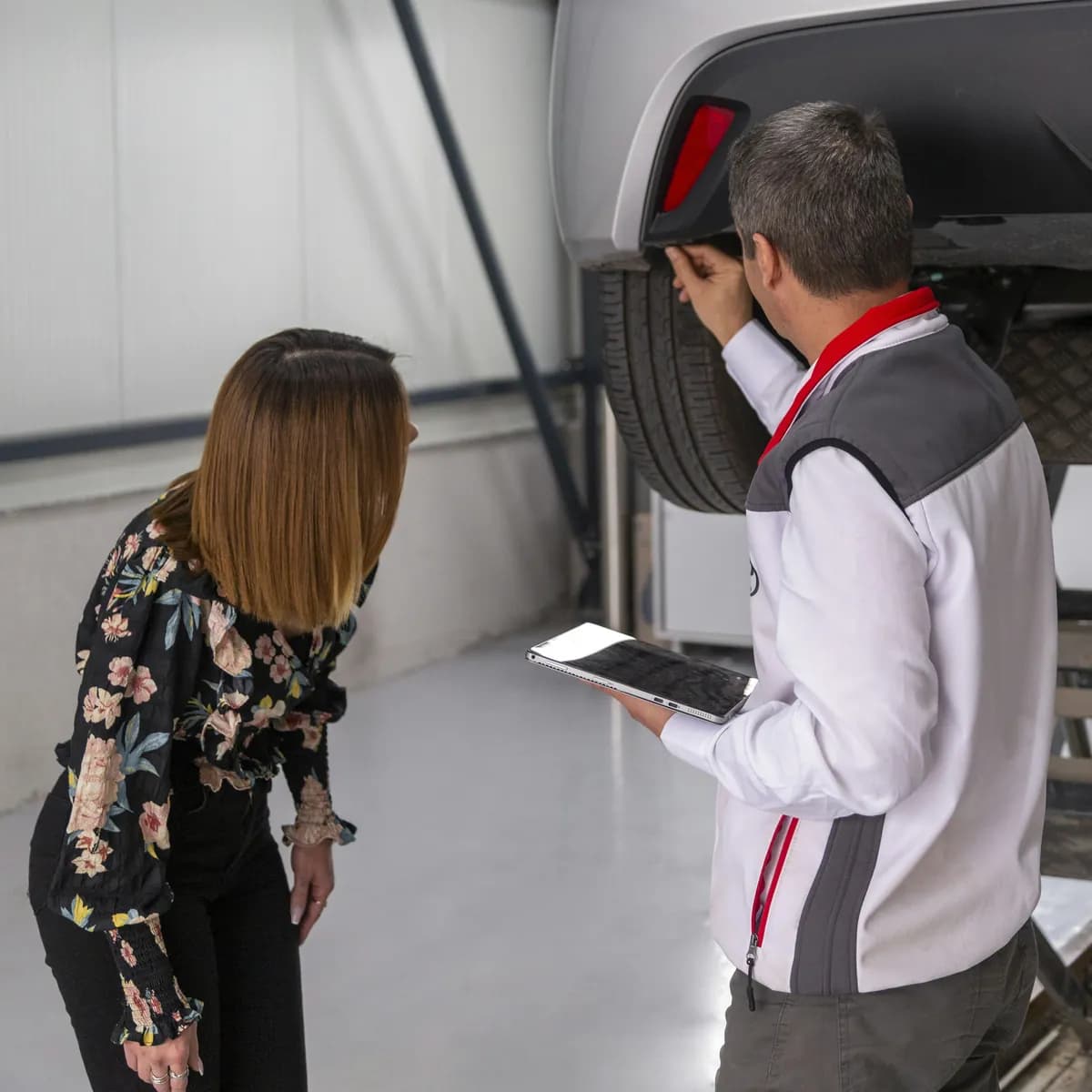 Een garagist toont een klant haar wagen op de brug en overloopt het werk op een tablet